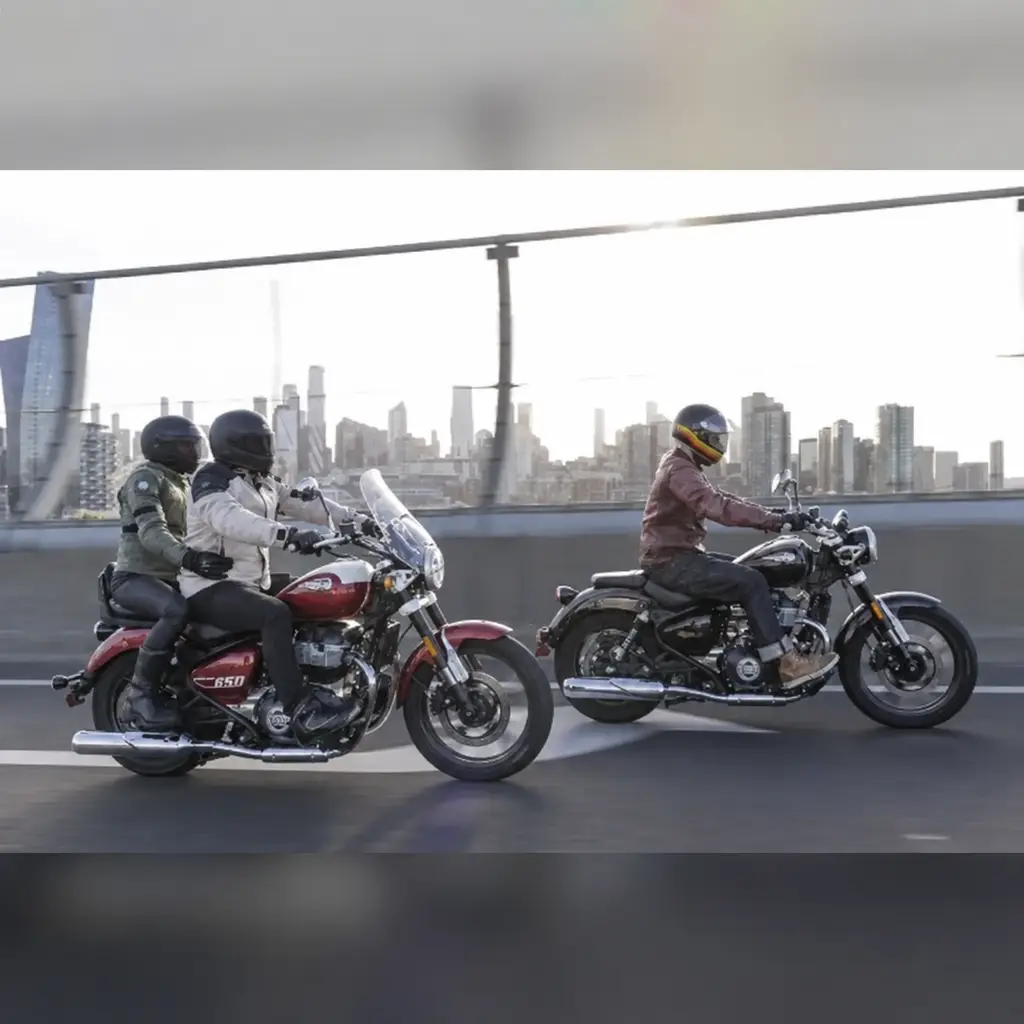Royal Enfield Super Meteor 650 mit Fahrer und Beifahrer sowie geschlossenen Helmvisieren auf einer Stadtbrücke neben einem zweiten Motorrad